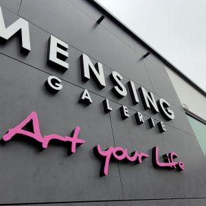 Logo Mensing Galerie "Art your Life" auf dunkler Außenwand montiert