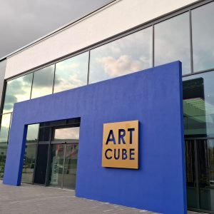 Goldlackiertes Art Cube Logo auf blauer Außenwand