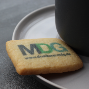 Keks mit Log MDG neben schwarzer Tasse